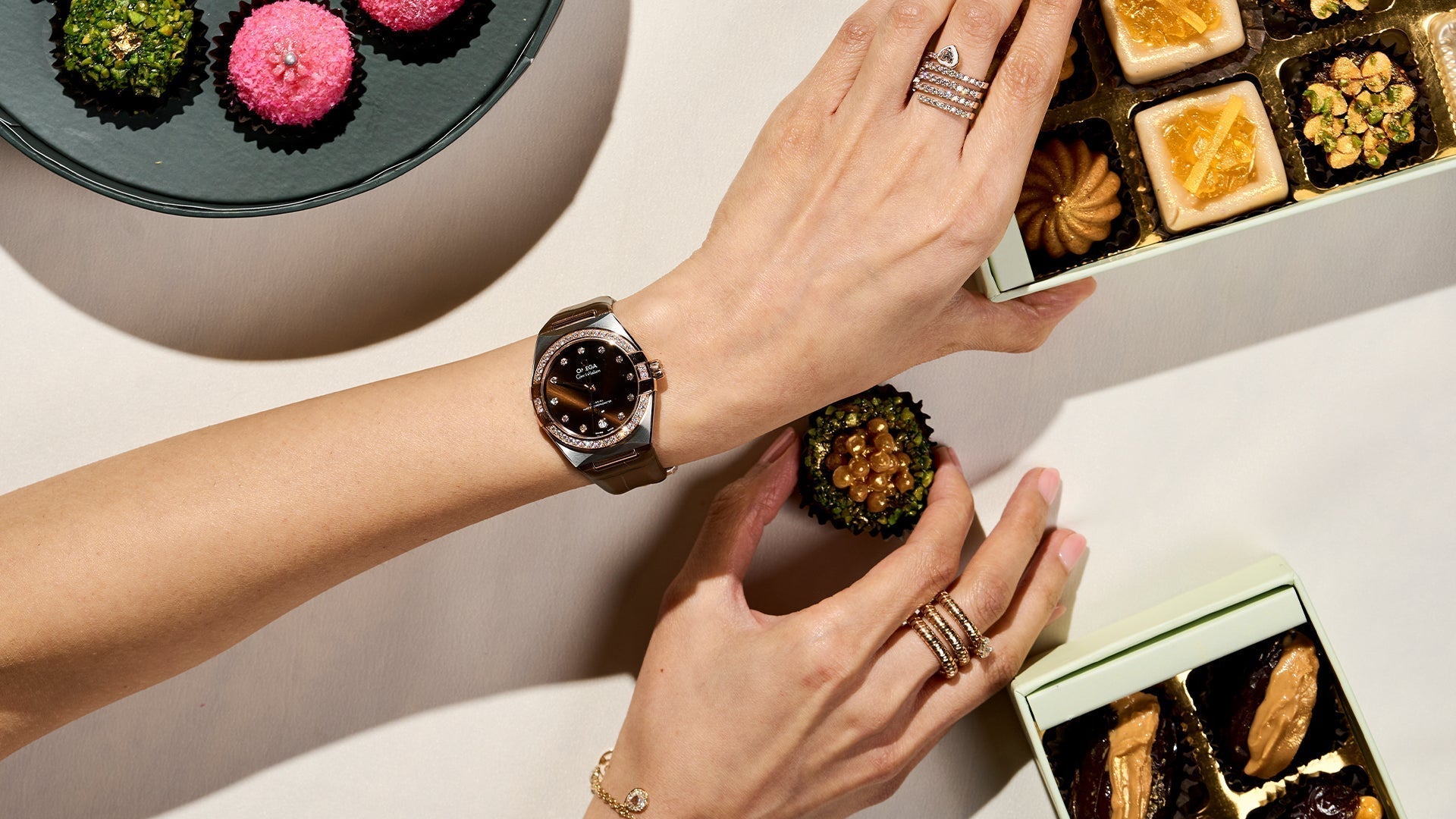 Woman wearing an Omega Constellation watch while enjoying Diwali sweets – luxury wristwatch styling for festive occasions with diamond rings and elegant Indian desserts.